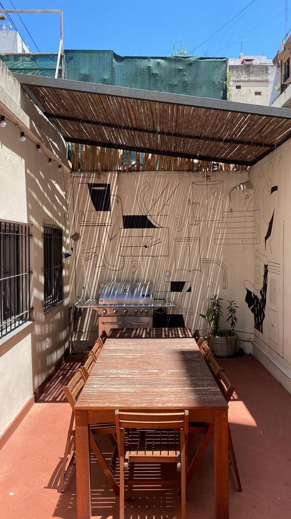 Patio con parrilla y mesa para 10 personas, mural decorativo y luces colgantes — donde se cierra el viernes con un asado